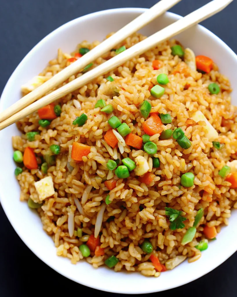A bowl of Chinese fried rice featuring fluffy rice grains, green peas, diced carrots, and chopped green onions, served with wooden chopsticks. This Chinese fried rice recipe is a classic Asian dish, perfect for a quick and healthy meal.