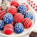 Red, white, and blue Oreo balls decorated with patriotic sprinkles and star-shaped toppings on a white plate, with one ball cut open revealing dark chocolate Oreo filling.