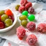 A colorful assortment of Jolly Rancher candied grapes and frozen grapes on parchment paper, with a bowl of shiny, glazed grapes.