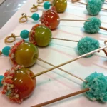 Skewered Jolly Rancher candy grapes coated with colorful sugar crystals and rock candy, arranged on a white surface.