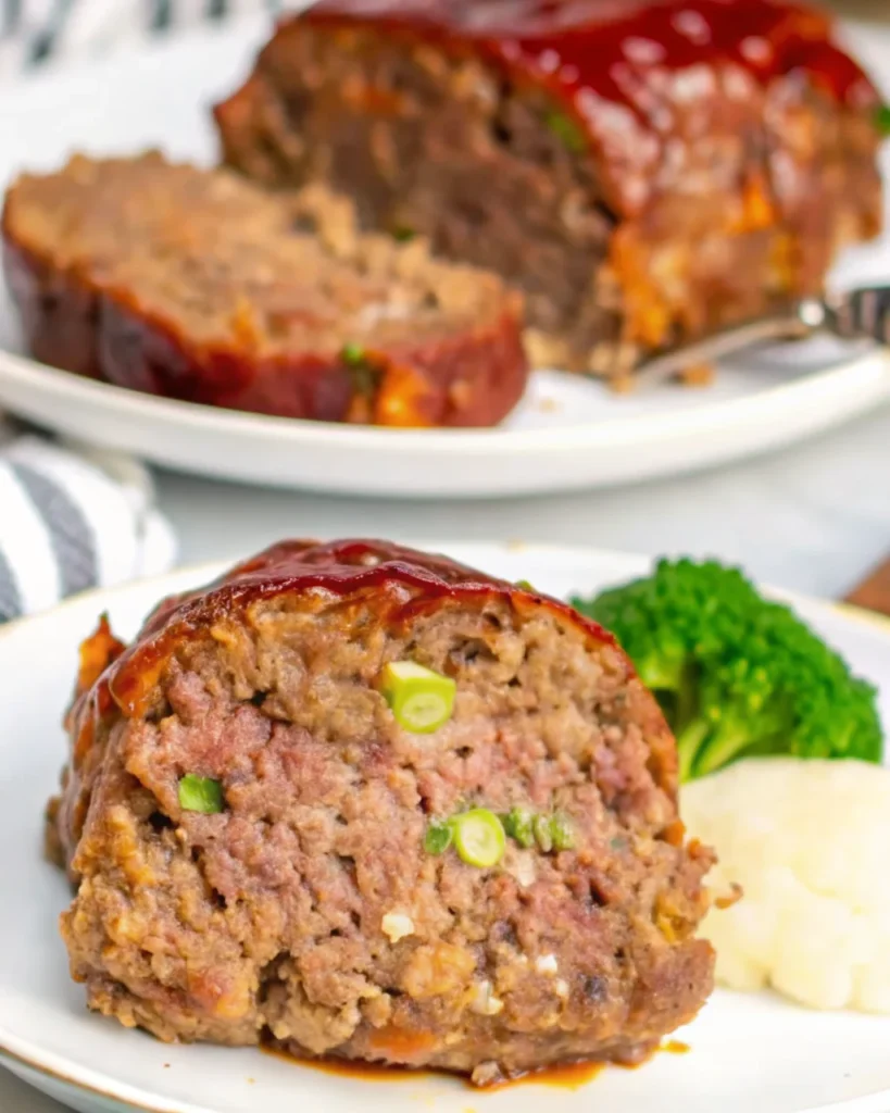 A slice of Cracker Barrel meatloaf topped with a glossy, rich ketchup glaze on a white plate, garnished with fresh parsley.