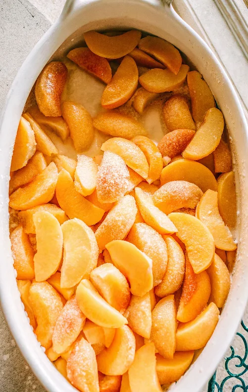 Fresh peach cobbler with golden brown biscuit topping and bubbling fruit filling served in white baking dish with vanilla ice cream scoop