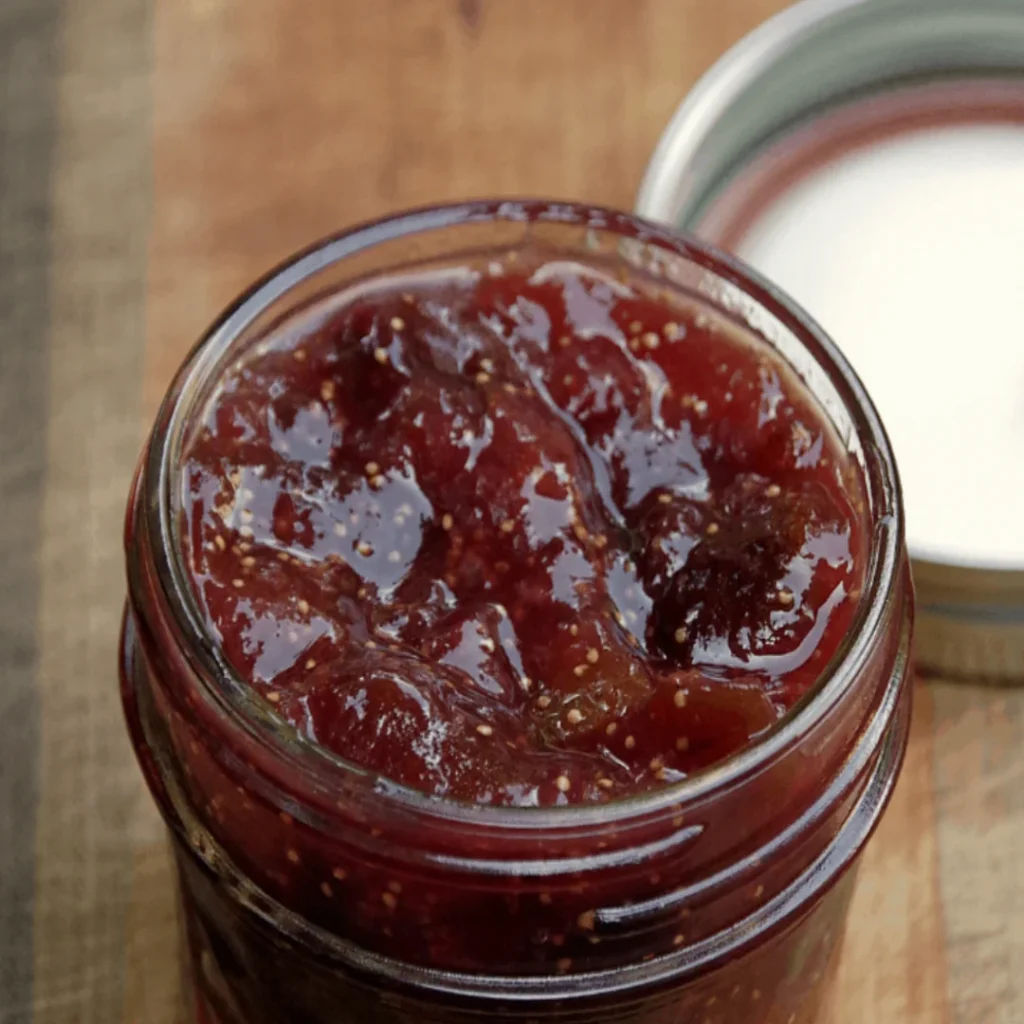 Homemade fig jam recipe in glass jar showing chunky texture with fig seeds and pieces on wooden surface