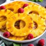 Grilled pineapple rings served on a white plate with fresh raspberries, showcasing caramelized edges and juicy tropical texture.