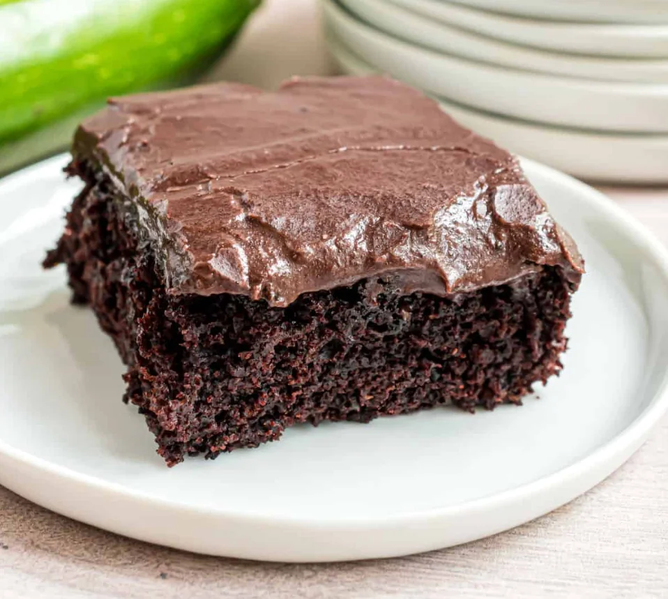 Fudgy chocolate zucchini brownie topped with rich chocolate frosting on a white plate.