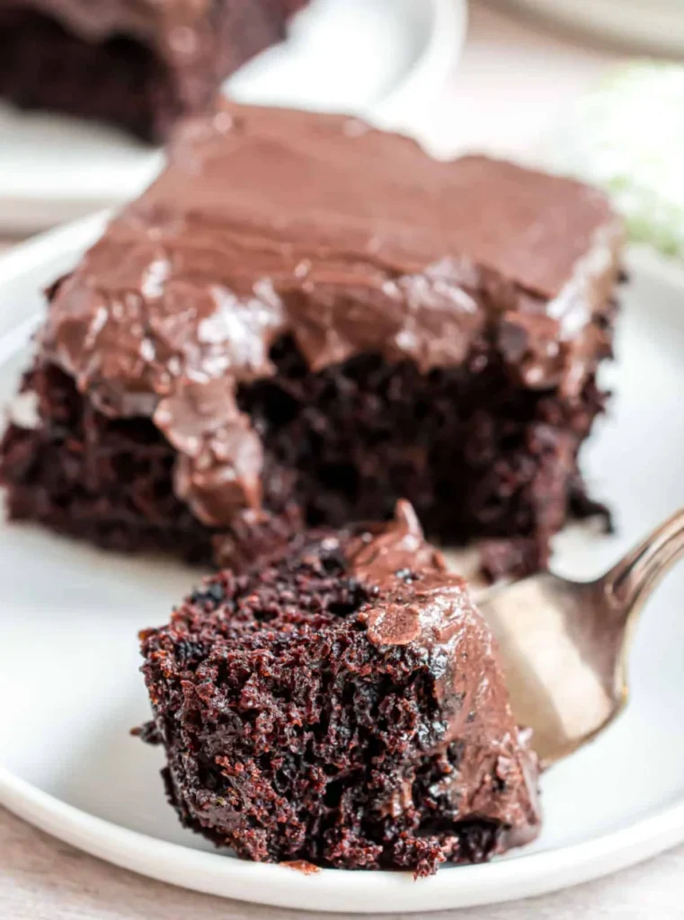 Fudgy chocolate zucchini brownie topped with rich chocolate frosting on a white plate.