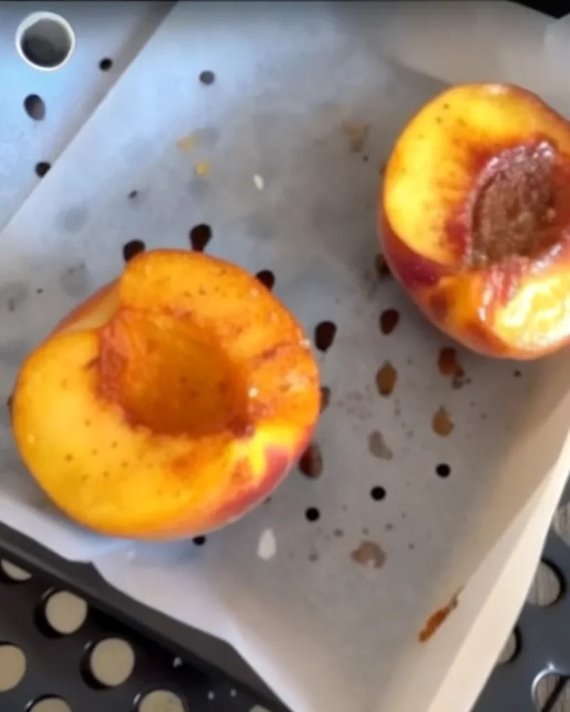 Air fryer peaches served with a scoop of vanilla ice cream, sprinkled with cinnamon and brown sugar in a ceramic bowl.