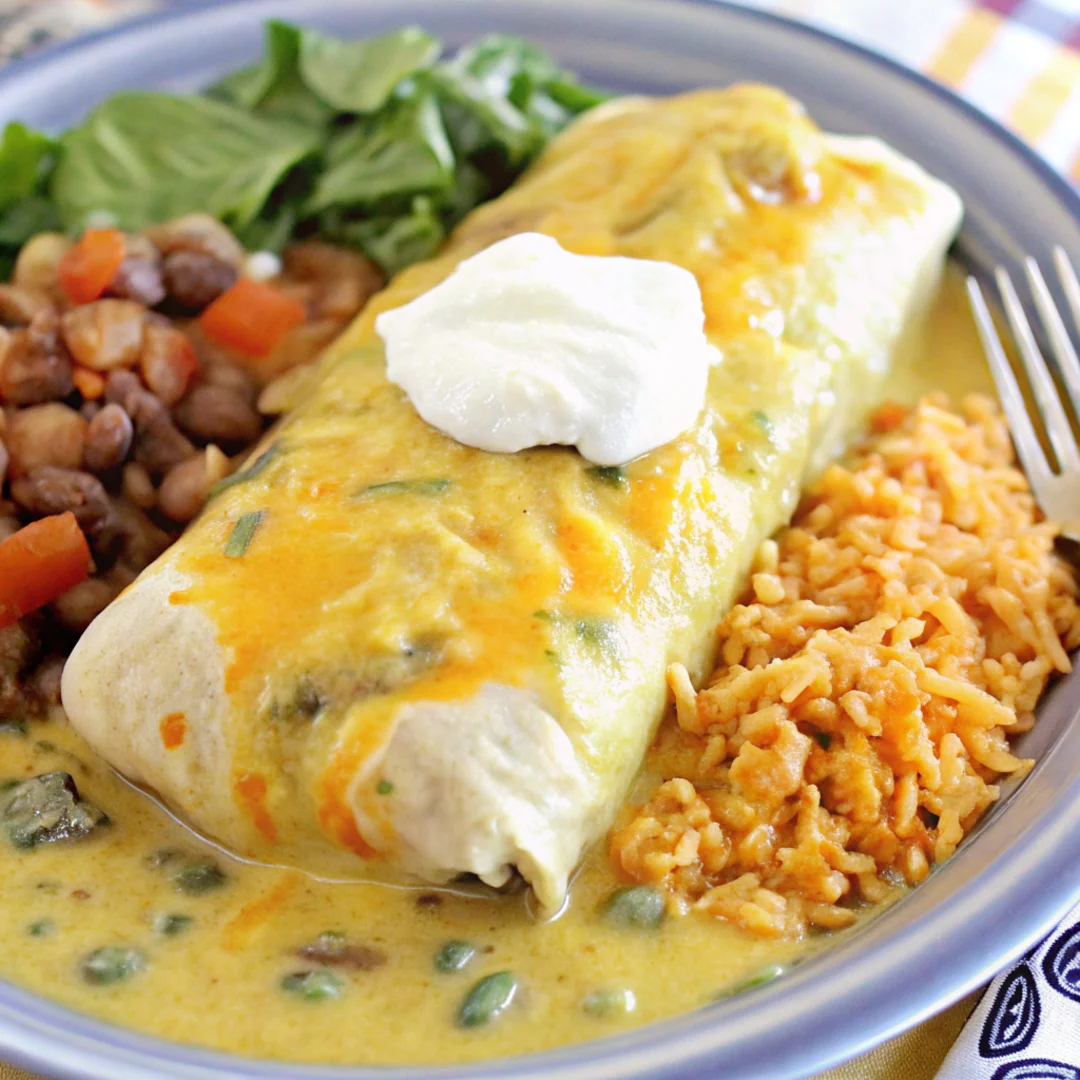 Smothered green chili burrito topped with melted cheese and sour cream, served with Mexican rice, beans, and fresh greens.