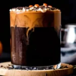 A close-up of a glass of cold brew coffee topped with creamy pumpkin spice cold foam, decorated with colorful Halloween sprinkles, showcasing the perfect fall-inspired beverage.