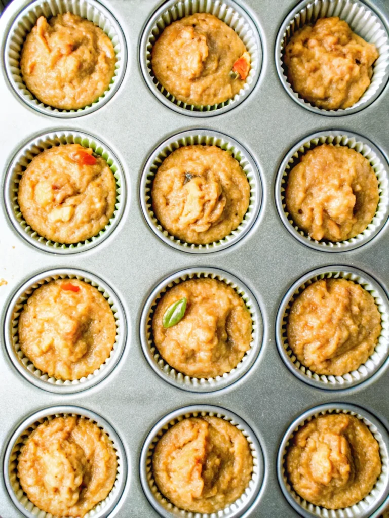 Fluffy whole wheat zucchini carrot muffin with a golden-brown top, set on a marble surface with a cooling rack in the background.