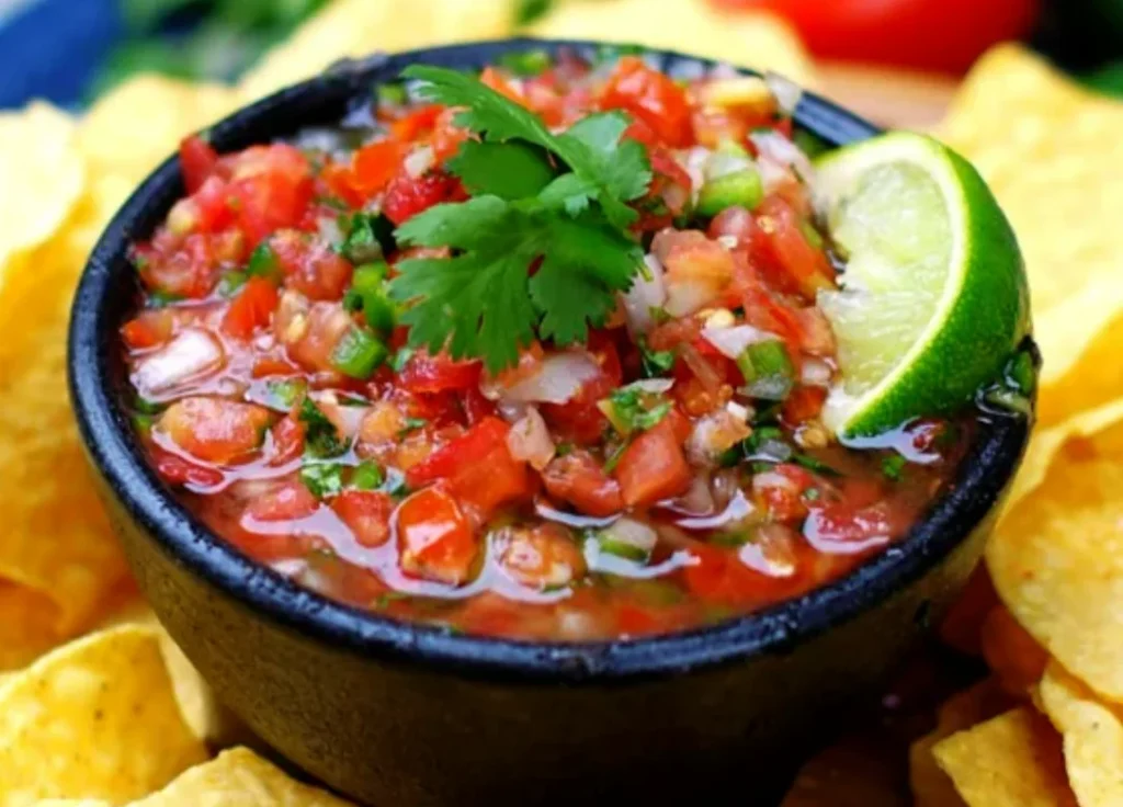 Fresh salsa with cilantro lime recipe—bowls of chunky salsa made with fresh tomatoes, onions, jalapenos, and cilantro, garnished with a tortilla chip and lime.