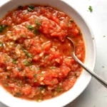Fresh salsa made with tomatoes, cilantro, jalapenos, and lime juice in a white bowl, garnished with fresh herbs.