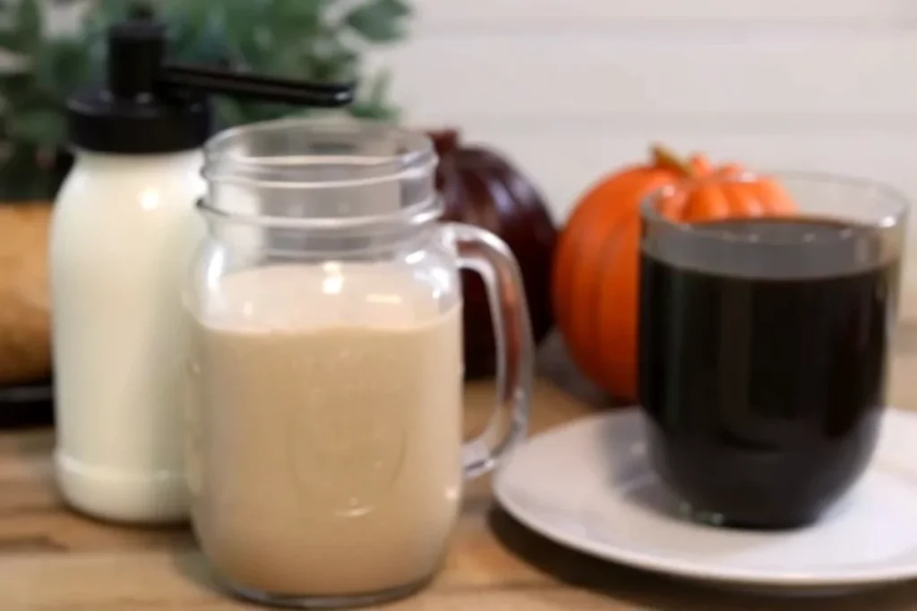 Homemade pumpkin coffee creamer in mason jar with fresh coffee cup and orange pumpkin on kitchen counter