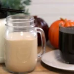 Homemade pumpkin coffee creamer in mason jar with fresh coffee cup and orange pumpkin on kitchen counter