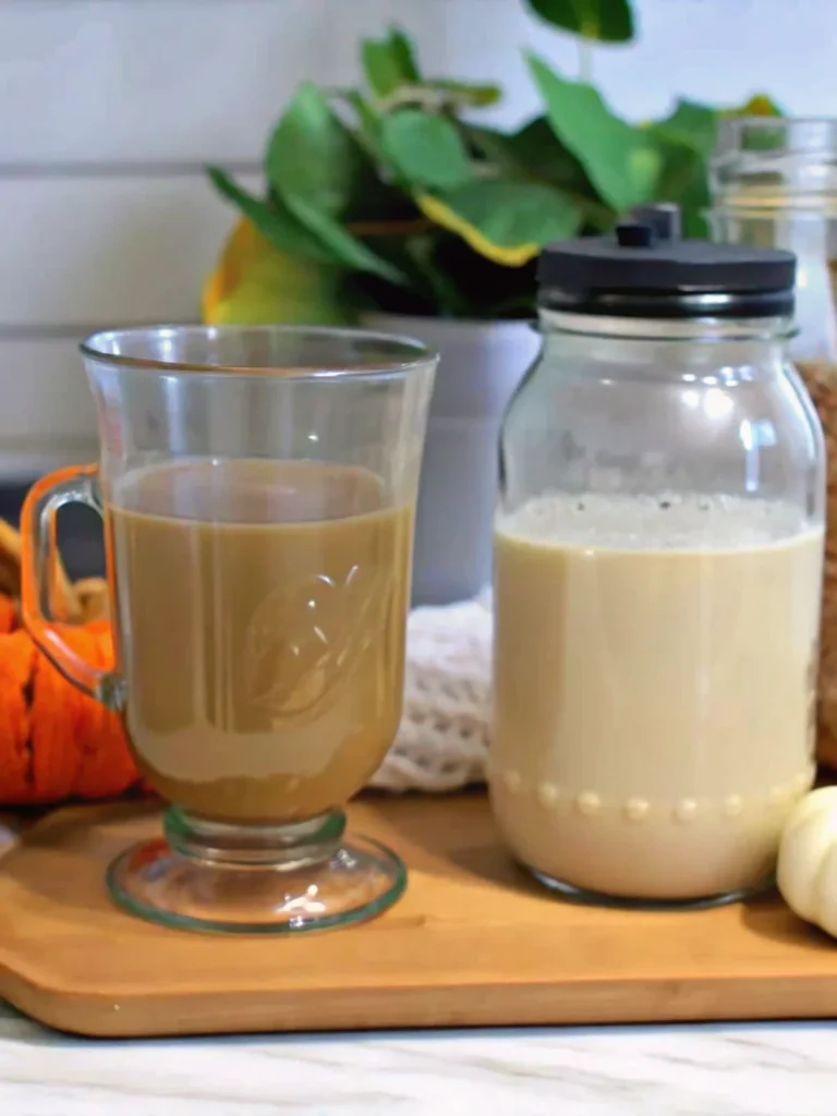 Homemade pumpkin coffee creamer in mason jar with fresh coffee cup and orange pumpkin on kitchen counter
