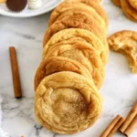 Golden pumpkin snickerdoodle cookies arranged on marble surface with cinnamon sticks - soft chewy fall cookies with pumpkin spice coating