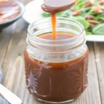 balsamic vinaigrette being drizzled from wooden spoon into glass jar with fresh salad greens in background