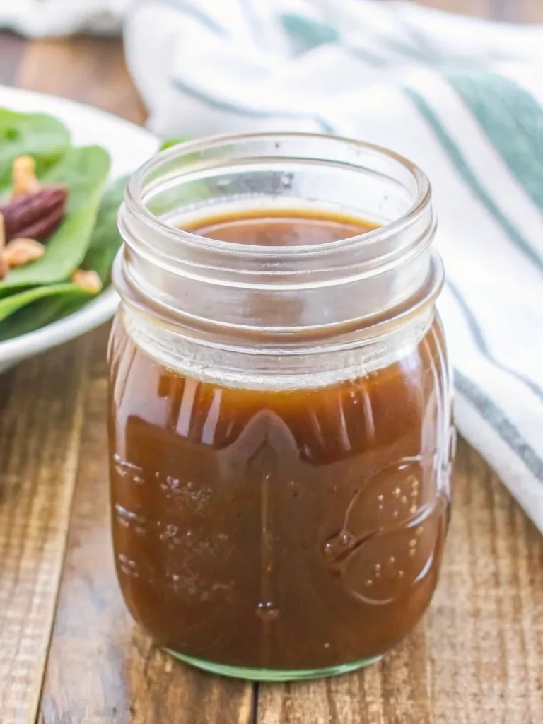 balsamic vinaigrette being drizzled from wooden spoon into glass jar with fresh salad greens in background