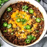 Texas style chili recipe served in white bowl topped with melted cheese, sliced jalapeños, and fresh cilantro