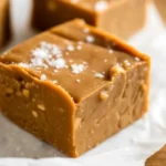 Homemade salted caramel fudge squares topped with sea salt crystals on parchment paper