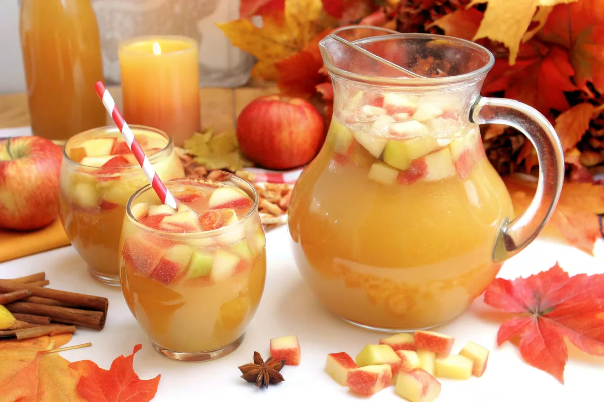 Refreshing autumn apple cider sangria in a pitcher and glasses with diced apples, surrounded by fall leaves and spices.