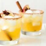 Fall apple cider cocktail with cinnamon stick, star anise, and apple slice garnish in a cinnamon-sugar rimmed glass.