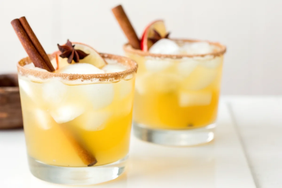 Fall apple cider cocktail with cinnamon stick, star anise, and apple slice garnish in a cinnamon-sugar rimmed glass.