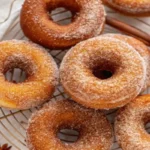 Golden-brown baked pumpkin donuts with cinnamon sugar coating arranged on white plate with autumn spices in background