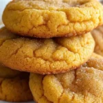 Soft pumpkin sugar cookies with cream cheese frosting arranged on parchment paper, showing golden edges and fluffy texture