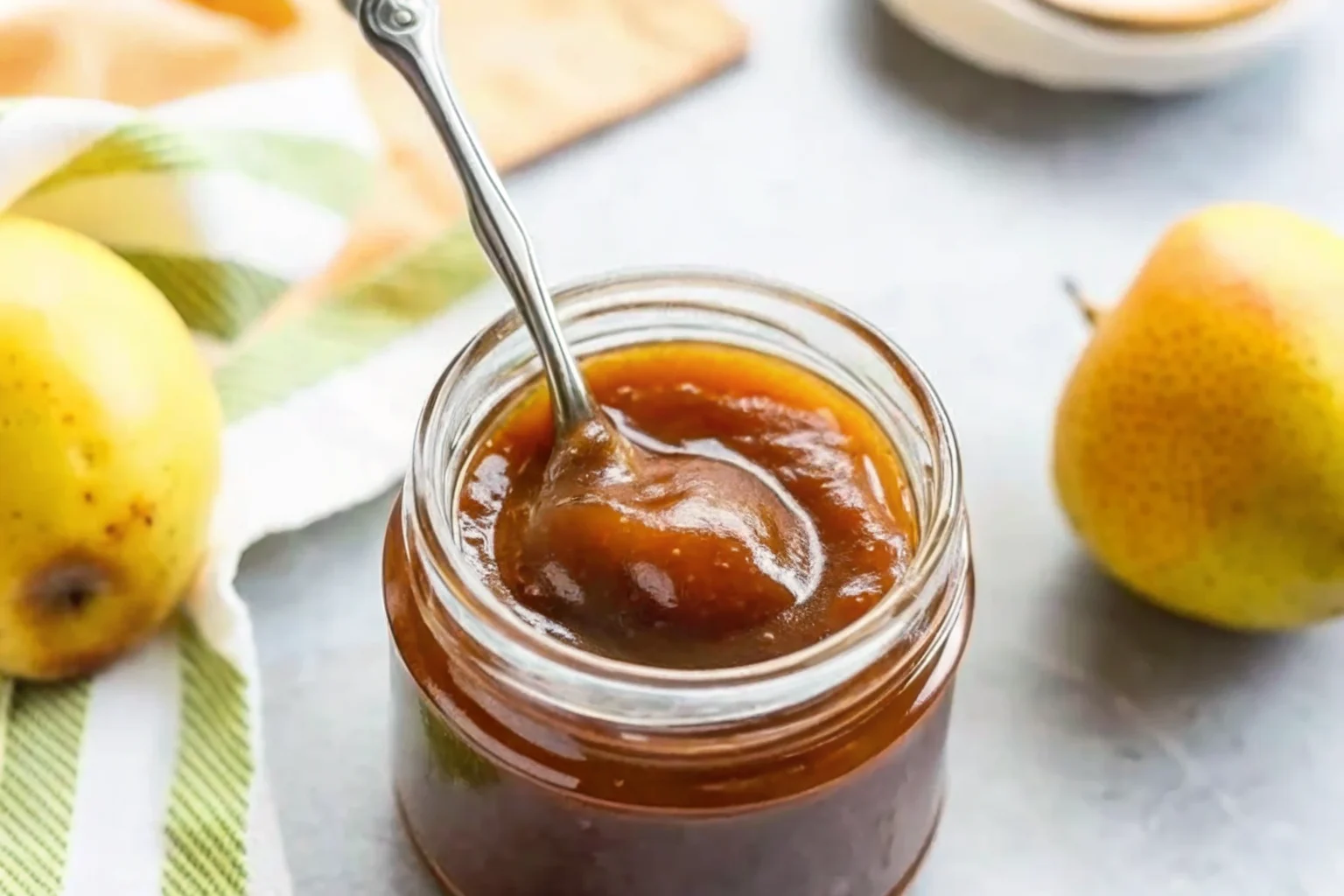 Homemade pear butter recipe in glass jars with fresh Bartlett pears, cinnamon sticks, and warm spices arranged on rustic wooden cutting board, showing the smooth golden-brown texture of the finished pear butter spread