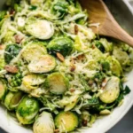 Fresh shaved Brussels sprout salad with Parmesan cheese and red wine vinaigrette in a white bowl, showing delicate green ribbons of raw Brussels sprouts