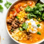 Creamy taco soup in white bowl topped with shredded cheese, sour cream, cilantro and avocado slices on wooden table