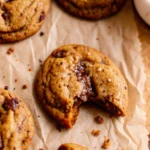 Brown butter pumpkin cookies with chocolate chips on parchment paper, showing golden-brown edges and perfectly round shape with pools of melted chocolate