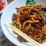 Quick and flavorful beef black pepper udon noodles served in ceramic bowl with chopsticks and garnish