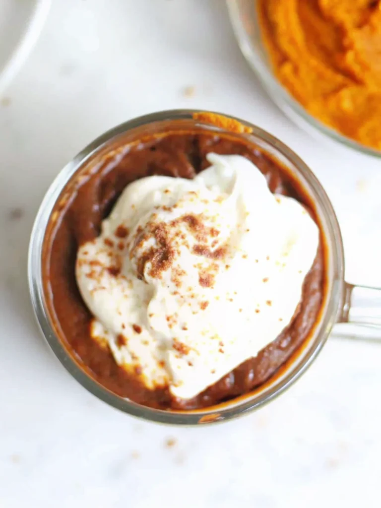 Creamy Pumpkin Spice Hot Chocolate in white mug topped with whipped cream and cinnamon, surrounded by fall decorations and pumpkin spice ingredients