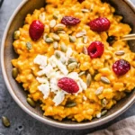 Creamy baked pumpkin risotto with goat cheese, cranberries, and pumpkin seeds in elegant white bowl, garnished with fresh sage