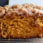 Freshly baked pumpkin bread with golden streusel topping and maple glaze drizzle on wooden cutting board