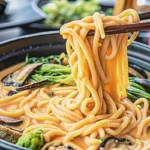 Creamy miso udon noodles in ceramic bowl topped with green onions and sesame seeds on wooden table