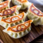 Golden crispy gyoza Japanese dumplings with pleated edges on white plate with soy sauce dipping bowl showcasing japanese recipe ideas