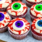 Spooky Halloween eyeball cupcakes with red velvet base, white buttercream frosting, realistic fondant eyeballs, and blood-red veins dripping down the sides
