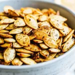 Golden brown salted roasted pumpkin seeds spread on parchment paper showing perfect crispy texture from this easy pumpkin seeds recipe