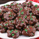 Crock pot candy chocolate peanut clusters cooling on parchment paper with slow cooker in background