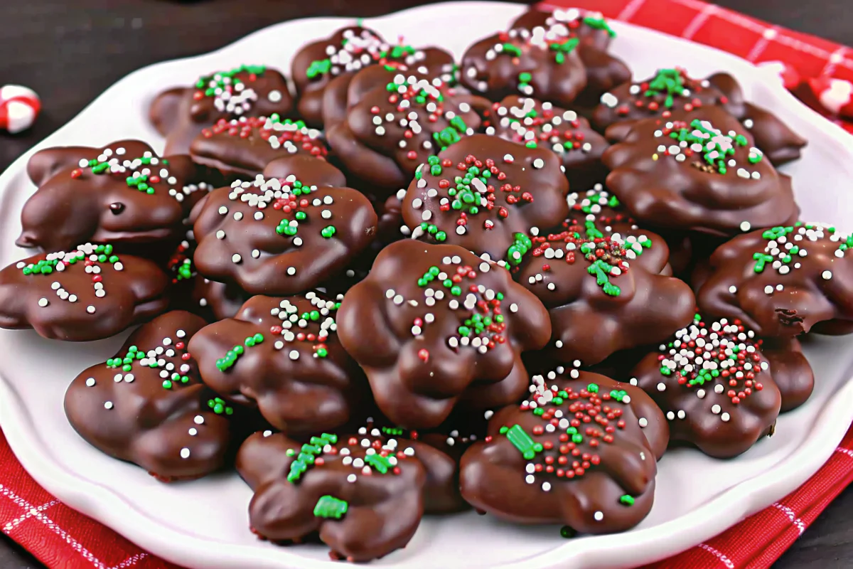 Crock pot candy chocolate peanut clusters cooling on parchment paper with slow cooker in background