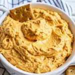 Creamy pumpkin dessert dip for fall parties served in orange bowl with graham crackers and apple slices