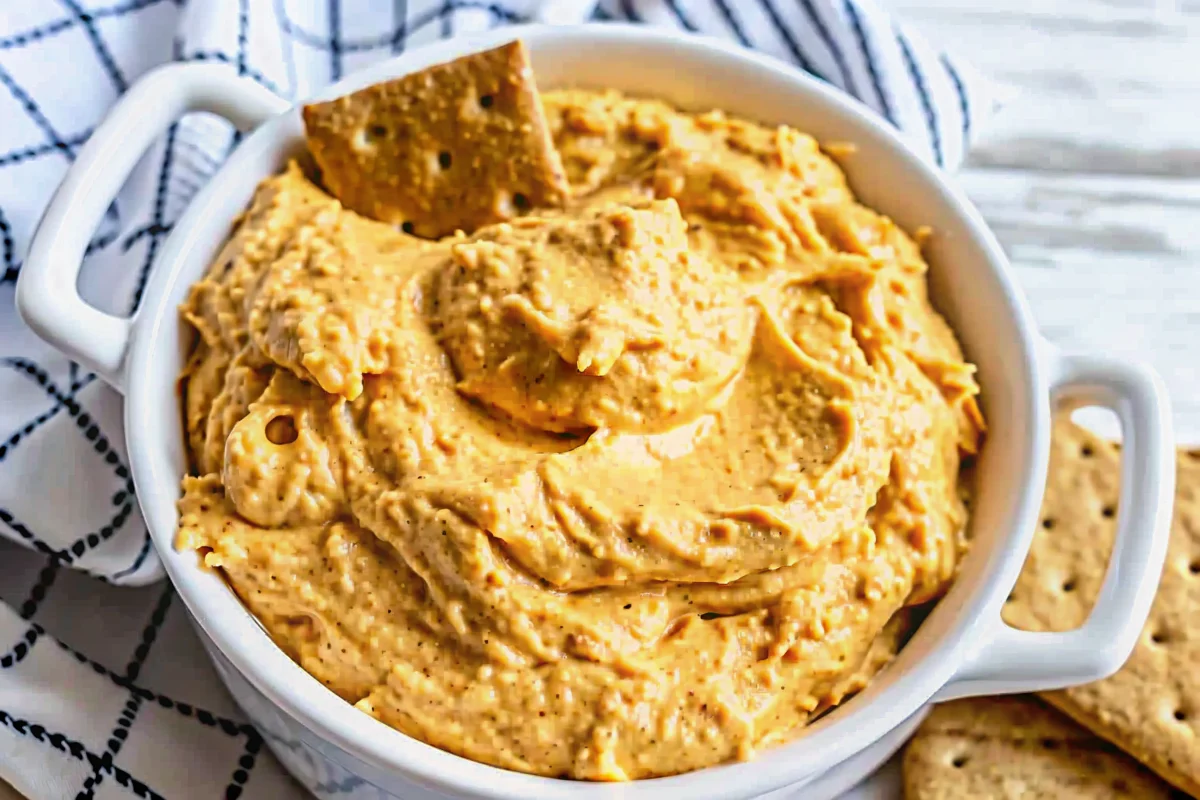 Creamy pumpkin dessert dip for fall parties served in orange bowl with graham crackers and apple slices