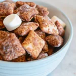 Homemade Smores Chex Mix spread on parchment paper showing chocolate-coated cereal squares mixed with mini marshmallows and dusted with powdered sugar