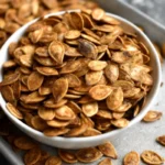 Golden cinnamon sugar roasted pumpkin seeds spread on parchment paper showing perfectly crispy texture from homemade pumpkin seeds recipe