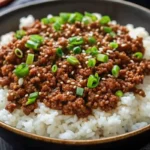 Korean ground beef bowl with seasoned rice, garnished with green onions and sesame seeds in a white ceramic bowl