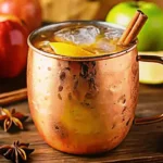 refreshing Apple Cider Mule Non Alcoholic Drink in a copper mug, garnished with a fresh apple slice and a cinnamon stick on a rustic wooden surface.