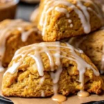 Golden brown copycat Starbucks pumpkin scones with vanilla and pumpkin spice glaze drizzled on top, arranged on parchment paper
